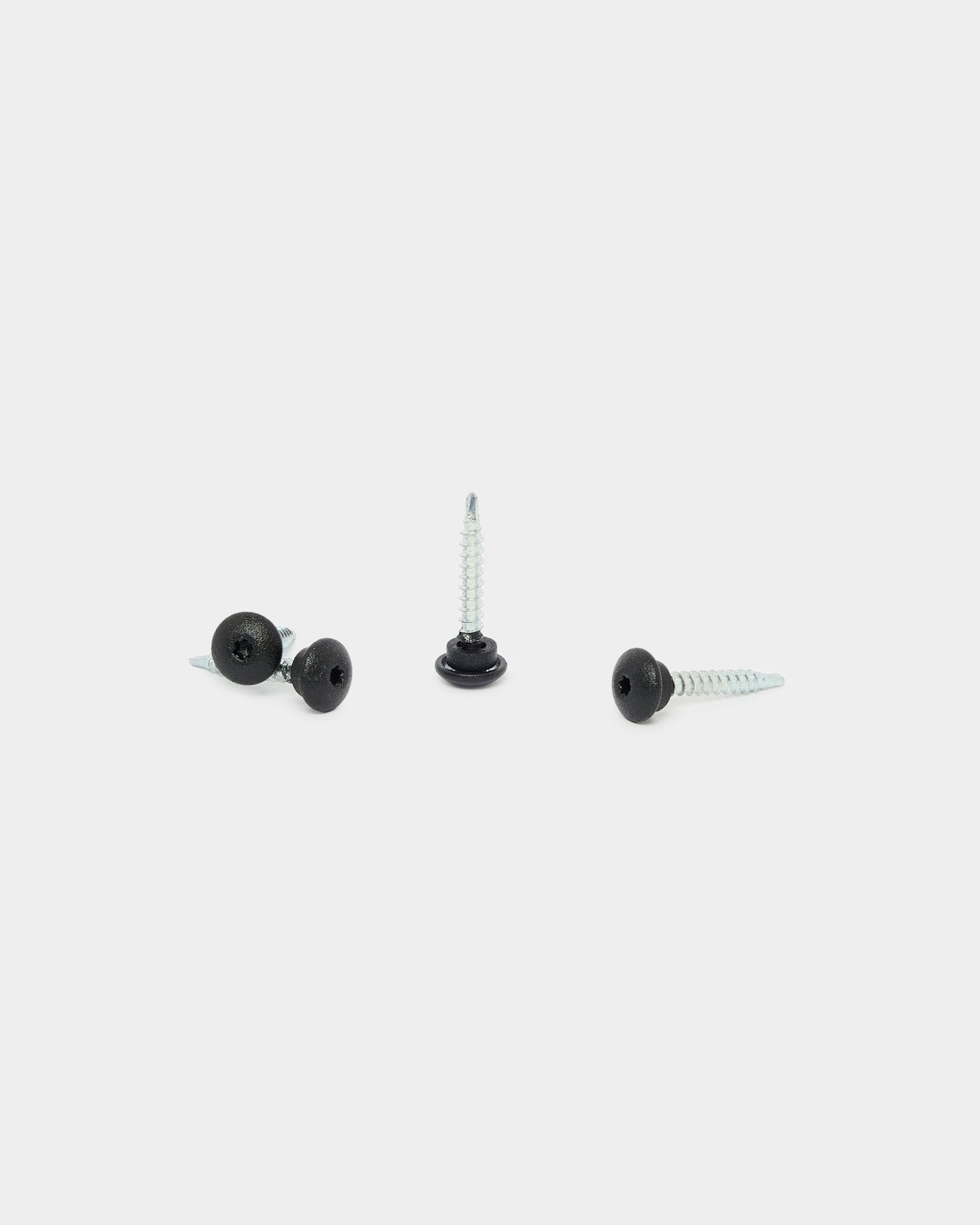 Tre WoodUpp black 4,8x35 frontskruer med Ø9,5 skiver, laget for Akupanel akustikkpaneler, på hvit bakgrunn: én stående, to liggende.